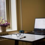 Study setup with a laptop, glasses, whiteboard, and marker on a desk next to a window.